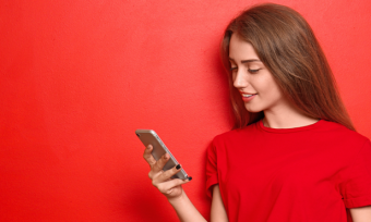 Young woman looking at phone in front of red background