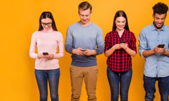 Four people holding and looking at mobile phones against yellow background