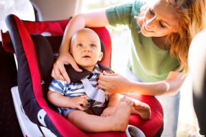 Young mother putting baby boy in the car seat