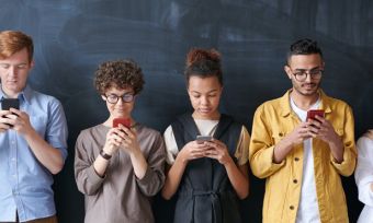 Group of people standing against dark wall looking at smartphones