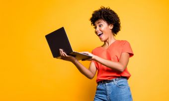 Young woman looking excitedly at computer against yellow background