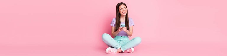 Woman sitting on floor looking at phone against light pink background