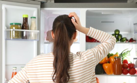 Woman staring into fridge, looking for something to eat