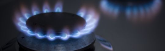 Gas stove top turned on with blue flame.