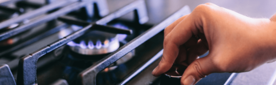 Hand turning dial on a gas stovetop.