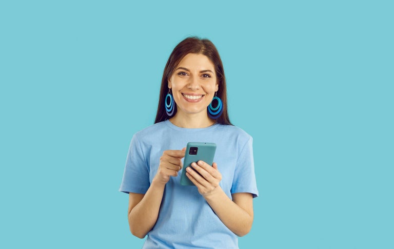 Woman smiling while holding her phone in front of a blue background.