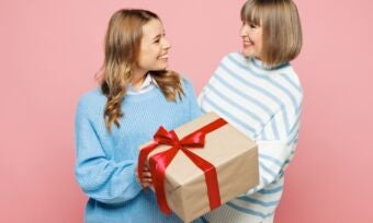 One younger woman and one older woman holding a giftbox with brown paper and red ribbon tied in a bow.