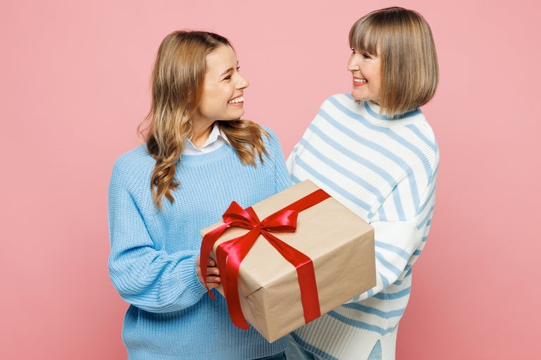 One younger woman and one older woman holding a giftbox with brown paper and red ribbon tied in a bow.